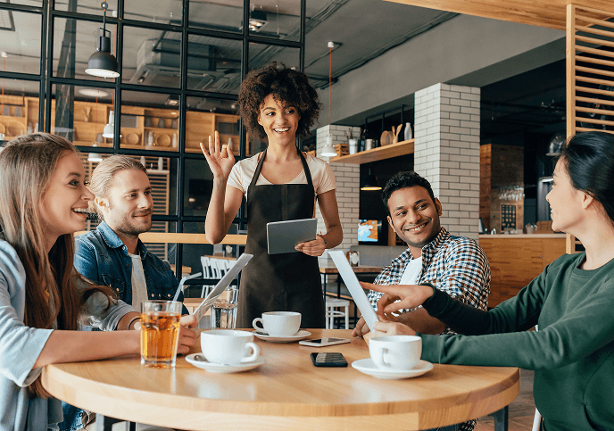 A group of people happily interacting with a waitress in a busy restaurant setting, enjoying coffee and conversation.